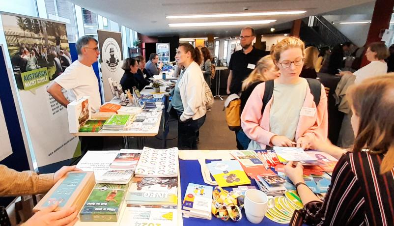 Tische mit Materialien zu Information und Vernetzung an Ständen von Austausch macht Schule und den Jugendwerken