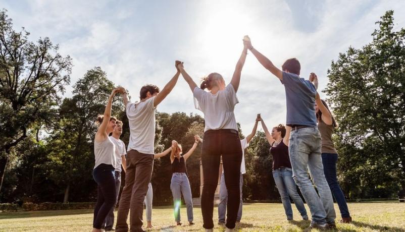 eine Gruppe Jugendlicher steht in einem Park und halten einander freundschaftlich