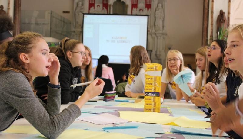 Deutsch-britische Schüler:innen beim gemeinsamen Workshop im Schulpartnerschaftsprogramm Jugendliche aus Deutschland und Großbritannien arbeiten gemeinsam an einem Tisch voller Notizen und Wörterbücher während eines Austausch-Workshops