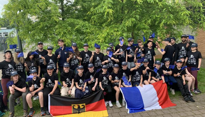 "Aux vélos | Auf die Räder" - deutsch-französische Schülerbegegnung Teilnehmende des Austauschprojekts "Aux vélos | Auf die Räder" sitzen und stehen im Park mit deutscher und französischer Fahne