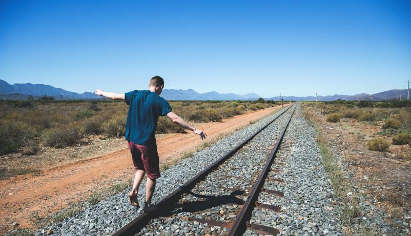  Junger Mensch balanciert tagsüber auf Bahngleisen - Symbol für Aufbruch und Auslandsaufenthalt.