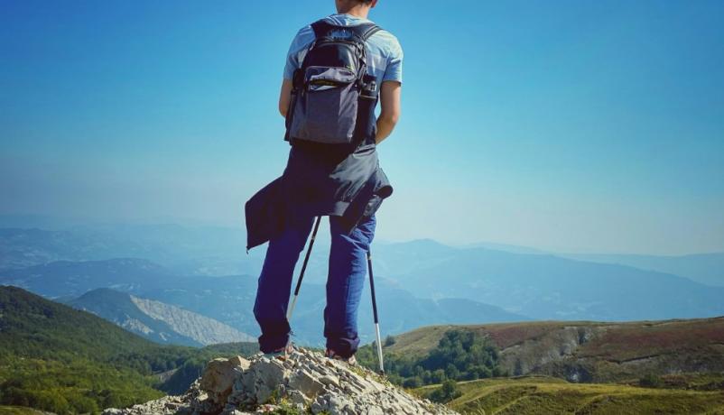 junger Mann steht auf einem Berg vor einem weiten Tal mit dem Rücken zur Kamera