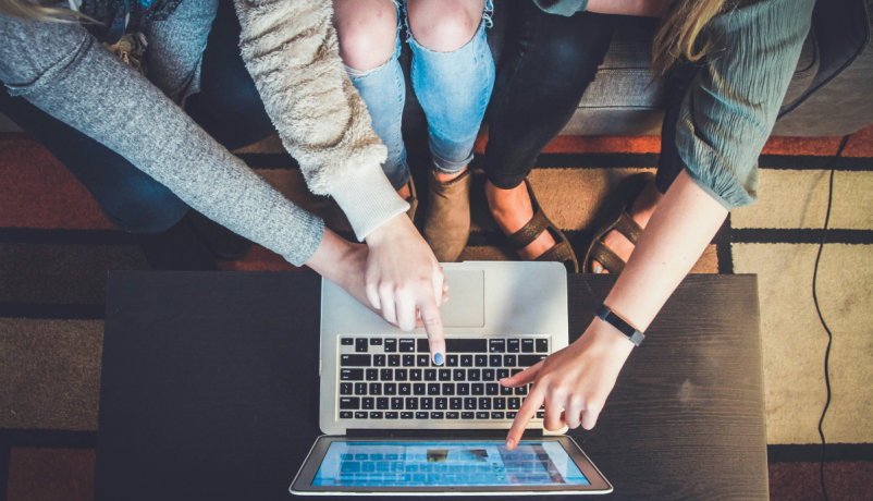 Drei junge Menschen deuten auf einen Laptop-Bildschirm