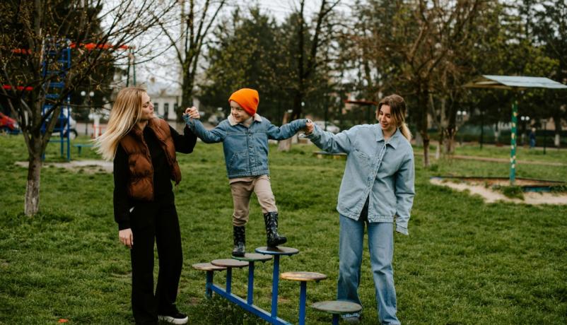 zwei Jugendliche halten ein Kind und helfen ihm auf einem Spielplatzgerät