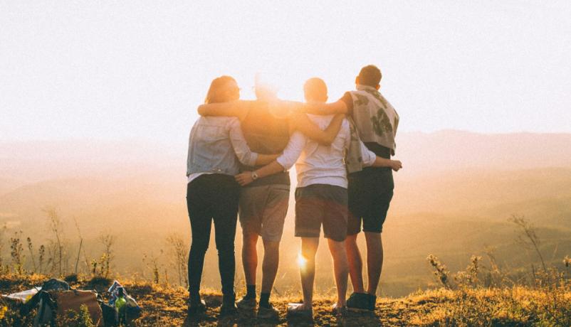 Vier Jugendliche halten sich an den Schultern umfasst im Sonnenuntergang