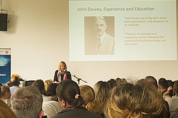 Dr. Julia Sattler spricht vor Publikum auf dem Fachtag schulischer Austausch NRW, im Hintergrund ist ein Zitat von John Dewey projiziert.