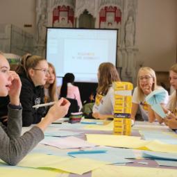 Jugendliche aus Deutschland und Großbritannien arbeiten gemeinsam an einem Tisch voller Notizen und Wörterbücher während eines Austausch-Workshops