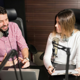 Zwei Personen mit Headsets sprechen in einem Radiostudio an einem Tisch vor Mikrofonen