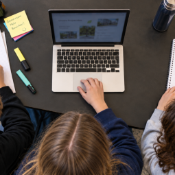 Die KI-generierte Illustration zeigt Schülerinnen und Schüler, wie sie an einem Laptop zu einem gemeinsamen Austauschprojekt arbeiten.