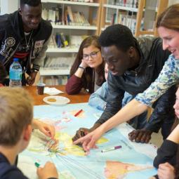 Gruppe Jugendlicher und Lehrerin erkunden Lerninhalte mit Weltkarte