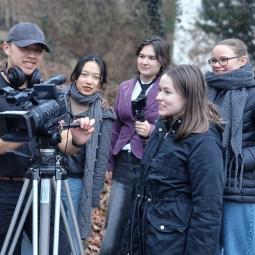 Gruppe junger Menschen bei einer Filmaufnahme im Freien; ein Teilnehmer bedient eine Videokamera