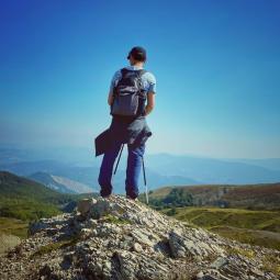 junger Mann steht auf einem Berg vor einem weiten Tal mit dem Rücken zur Kamera