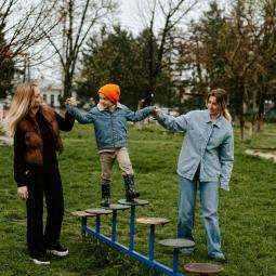 zwei Jugendliche halten ein Kind und helfen ihm auf einem Spielplatzgerät