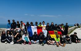 Internationale Begegnung "Aux vélos | Auf die Räder" – Jugendliche aus NRW und Frankreich am Cap Blanc-Nez (Ärmelkanal)  Jugendliche aus Lünen und Saint-Omer sitzen gemeinsam am Meer am Cap Blanc-Nez mit deutscher und französischer Fahne beim Austausch "Aux vélos | Auf die Räder"